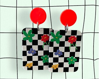 May include: A pair of checkerboard earrings with colourful flower designs. The earrings are made of red, white, black, green, blue, and yellow.