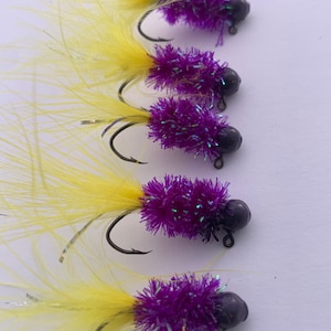 May include: Five purple and yellow fishing lures with black hooks and black beads. The lures are made of fluffy material and have a feather tail.
