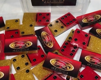 May include: A set of red and gold dominoes with a San Francisco 49ers logo. The dominoes are made of a glittery material.