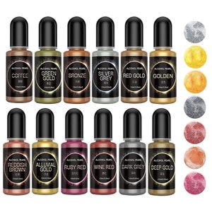 May include: Set of 12 alcohol ink bottles with pearlescent finishes. The bottles are labeled with the color names: Coffee, Green Gold, Bronze, Silver Grey, Red Gold, Golden, Reddish Brown, Alluvial Gold, Ruby Red, Wine Red, Dark Grey, and Deep Gold. Each bottle contains 10 ml of alcohol ink.