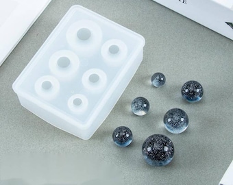 May include: A clear silicone mold with six round cavities for making resin spheres. Six finished resin spheres with a glittery, blue and black design are shown next to the mold.