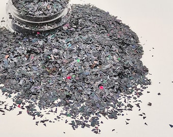 May include: A pile of iridescent black glitter flakes. The glitter is a mix of small and large pieces, and it has a subtle rainbow sheen.
