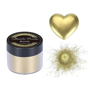 May include: A small jar of metallic bronze powder. The jar has a black lid and a clear glass body. The powder is a fine, shimmery gold color. The jar is labeled "Metallic Powder Bronze" and "Net Weight: 20ml".
