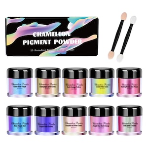 May include: Ten small jars of chameleon pigment powder, each with a different color combination. The jars are arranged in two rows of five. The colors are green-blue-purple, champagne gold-green, red-orange-yellow, golden blue-green, pinking rose-red-purple, blue-purple-red, purple-red-golden, purplish red-blue-green, purple blue-red-orange, and cream green-green. The jars are labeled with the color combinations. The image also includes two small white makeup sponges on black sticks.