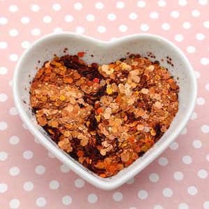 May include: A heart-shaped white bowl filled with copper glitter. The glitter is a mix of small and large pieces, with a variety of shapes and sizes.