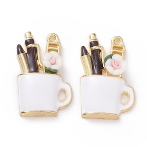 May include: Two gold-tone charm pendants featuring a white ceramic mug with a gold rim. Each mug contains three gold-tone pens and a pink flower.