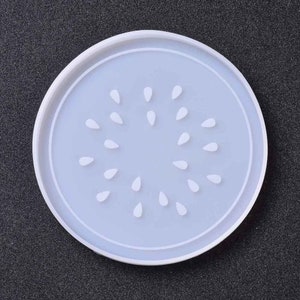 May include: White silicone coaster with a circular design of watermelon seeds. The coaster is approximately 10 cm in diameter.