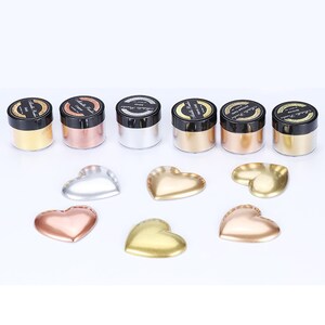 May include: Six small jars of metallic powder in gold, silver, copper, and rose gold colors. The jars are labeled "Metallic Powder".  There are also six heart-shaped samples of the metallic powder in the same colors.