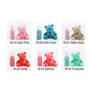 May include: Ten small bottles of paint with a geometric bear figurine next to each bottle. The bottles are labeled with the brand name "MORANDI" and the color name. The colors are light pink, dark cyan, warm grey, coral, salmon, and turquoise.