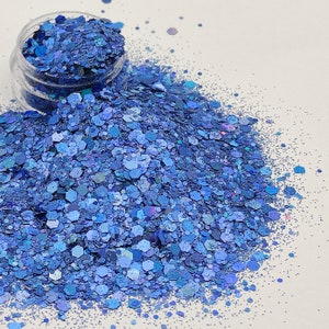 May include: A close-up of a pile of blue iridescent glitter. The glitter is scattered on a white surface.