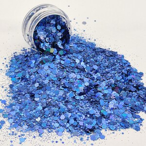 May include: A jar of blue iridescent glitter, with a variety of sizes and shapes of glitter. The glitter is spilling out of the jar onto a white surface.