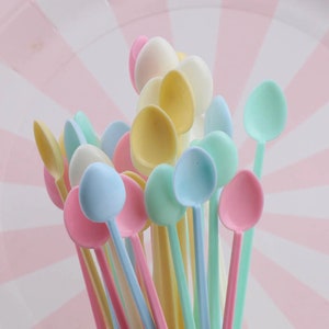 May include: A bunch of colorful plastic spoons in pastel shades of blue, yellow, pink, and white. The spoons are arranged in a fan shape, with the handles pointing upwards.