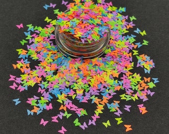 Könnte beinhalten: Ein Glas gefüllt mit buntem Schmetterlingsglitter. Der Glitter ist eine Mischung aus Neonrosa, Grün, Gelb, Blau und Orange.