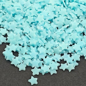 May include: A large quantity of light blue star-shaped sprinkles. The sprinkles are scattered on a black surface.