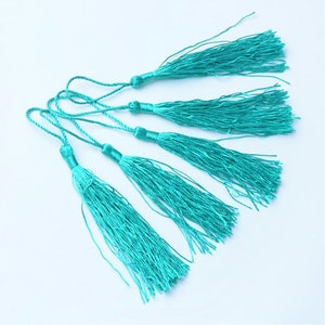 May include: Five turquoise blue tassels with long strands of fringe. The tassels are attached to thin cords.