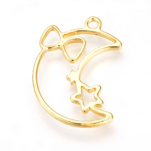 May include: Gold-toned metal charm featuring a crescent moon with a star and a bow. The charm has a hole at the top for attaching to a necklace or bracelet.