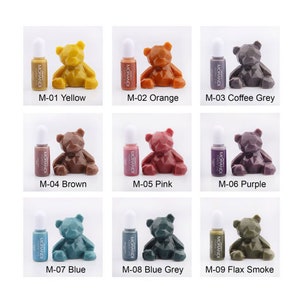 May include: Nine small bottles of paint with a teddy bear figurine in front of each bottle. The bottles are labeled with the color of the paint and the number M-01 through M-09. The colors are yellow, orange, coffee grey, brown, pink, purple, blue, blue grey, and flax smoke.