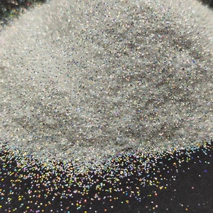 May include: A pile of iridescent white glitter with a rainbow sheen. The glitter is on a black surface.