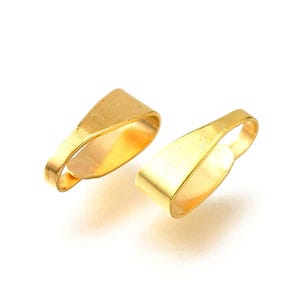 May include: Two gold-colored pendant bails, ideal for jewelry making. The bails have a curved, loop-like design for attaching to chains or cords. The metal has a smooth, reflective surface, and the bails are set against a white background.