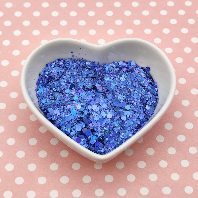 May include: A heart-shaped bowl filled with blue glitter. The glitter is a mix of different sizes and shapes, and it has a iridescent finish.