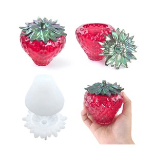 May include: A red glass strawberry-shaped jar with a green leaf lid. The jar is open and the lid is off to the side. There is also a white silicone mould of the same shape.