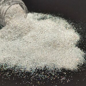 May include: A pile of iridescent white glitter, spilling out of a clear jar onto a black surface.