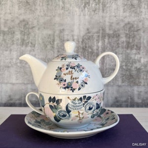May include: White ceramic teapot and teacup set with a floral pattern and the words "with love" in gold lettering. The teapot has a lid and a handle. The teacup has a handle and a saucer.