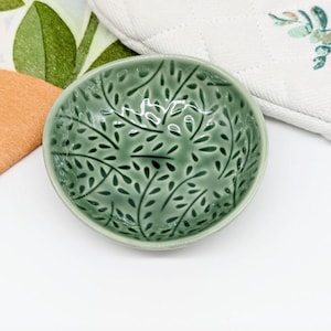 May include: A small, green ceramic bowl with a leafy pattern. The bowl is ideal for serving small snacks or dips.