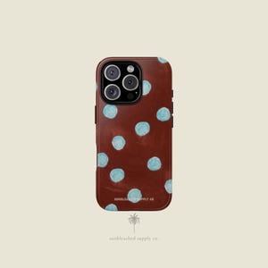 May include: A brown phone case with light blue polka dots. The case has a glossy finish and features a camera cutout. The text "SUNBLEACHED SUPPLY CO" is printed on the bottom of the case.