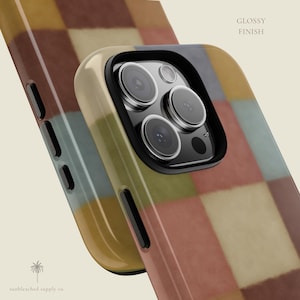 This phone case features a soft, muted checkerboard pattern made up of square blocks in earthy tones—dusty pink, cream, sage green, mustard yellow, brown, and light blue. Each square has a slightly textured, vintage look, creating a warm, cosy, quilt-like aesthetic. No additional graphics or text appear on the case the buyer receives.