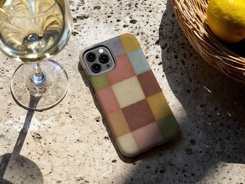 This phone case features a soft, muted checkerboard pattern made up of square blocks in earthy tones—dusty pink, cream, sage green, mustard yellow, brown, and light blue. Each square has a slightly textured, vintage look, creating a warm, cosy, quilt-like aesthetic. No additional graphics or text appear on the case the buyer receives.