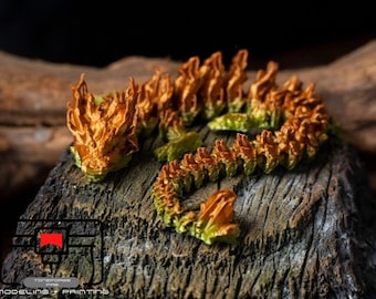 Può includere: Una statuetta di drago stampata in 3D di colore arancione e verde con una testa e una coda spigolose. Il drago è in posizione arrotolata su una superficie di legno.