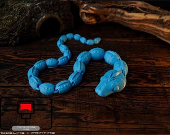 May include: A light blue, segmented snake toy made of plastic. The snake is curled up on a dark wood surface.