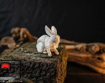 May include: A white 3D printed rabbit figurine sitting on a piece of tree bark. The rabbit is in a sitting position with its ears perked up.