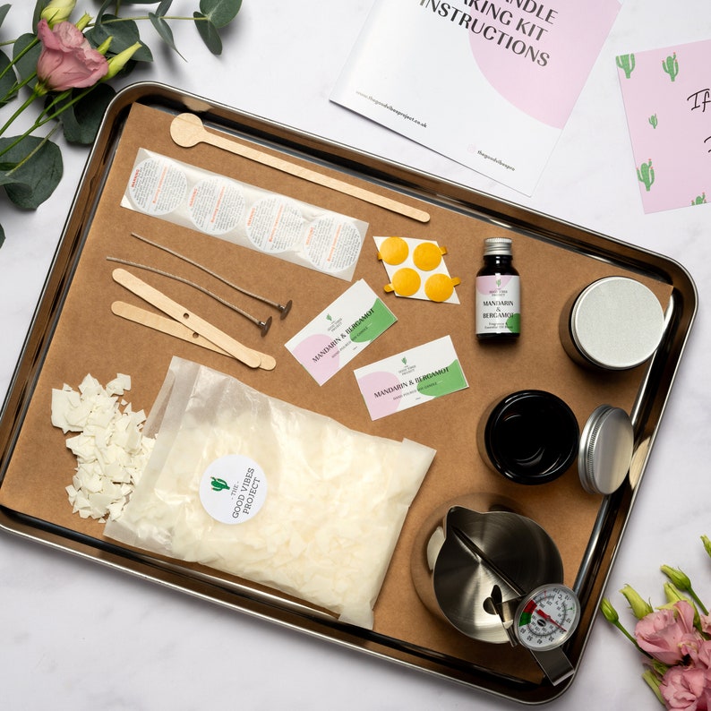 May include: A candle making kit with all the supplies needed to create your own candles. The kit includes wax flakes, wicks, essential oil, a metal pouring pitcher, a thermometer, and two jars. The kit also includes two cards with the text "Mandarin & Bergamot" printed on them.