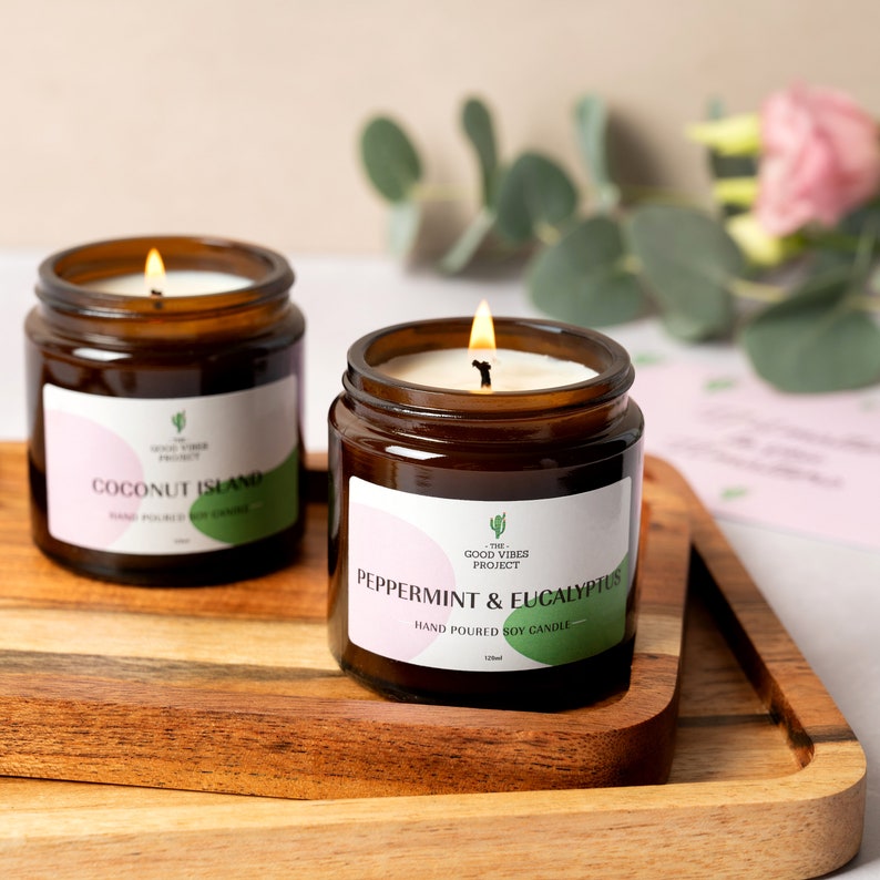 May include: Two amber glass candle jars with white labels. The candle on the left is labeled "Coconut Island" and the candle on the right is labeled "Peppermint & Eucalyptus". Both candles are hand-poured soy candles.