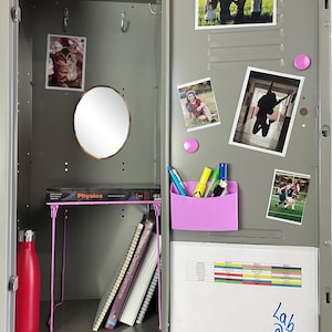 May include: Open gray metal locker with a pink shelf, a red water bottle, and a small round mirror. Inside are books, photos, and a pink pen holder with pens. The locker door has photos attached with magnets.