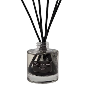 May include: A clear glass reed diffuser bottle with black reeds. The bottle has a label that reads "PIGGY & PANDA - Reed Diffuser - 100 ml". The reeds are inserted into the bottle.