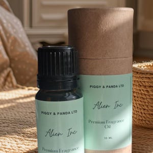 Op de afbeelding: Een kleine, donkere glazen fles met een zwarte dop en een cilindrische kartonnen container. Beide tonen de tekst "Alien Inc" en "Premium Fragrance Oil". De fles en container zijn gelabeld met "Piggy & Panda LTD" en bevatten 10 ml olie.
