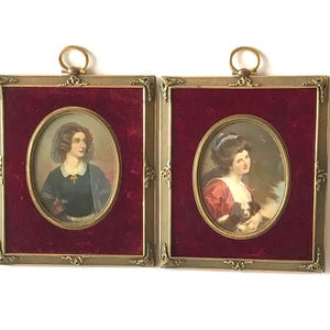 Peut inclure: Deux miniatures de portraits anciens dans des cadres dorés ornés. Chacune présente un portrait ovale sur un fond de velours rouge foncé. Les cadres ont des coins décoratifs et une boucle pour accrocher, mettant en valeur l'art vintage.