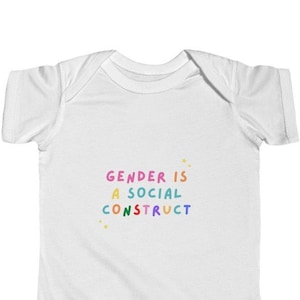 May include: White baby onesie with the text "GENDER IS A SOCIAL CONSTRUCT" in rainbow colors.