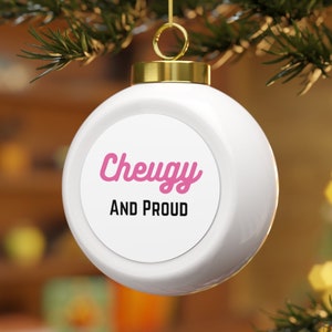 Puede incluir: Adorno navideño blanco con un círculo rosa que contiene el texto "Cheugy and Proud" en letras rosa y negras.
