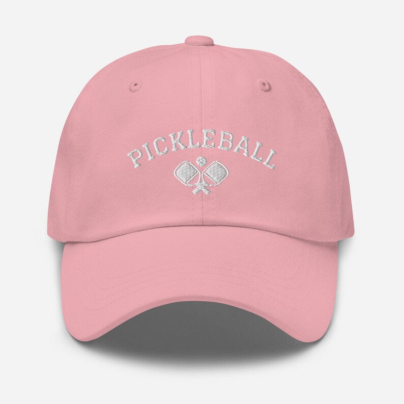 May include: A pink baseball cap with white embroidery that says "Pickleball" and features a pair of crossed pickleball paddles.