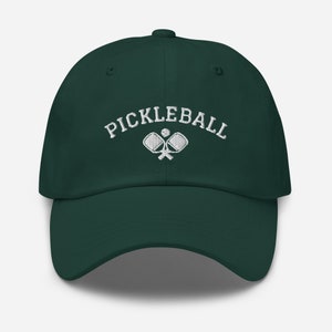 May include: A dark green baseball cap with white embroidery that reads "Pickleball" and features a pair of crossed pickleball paddles with a ball.
