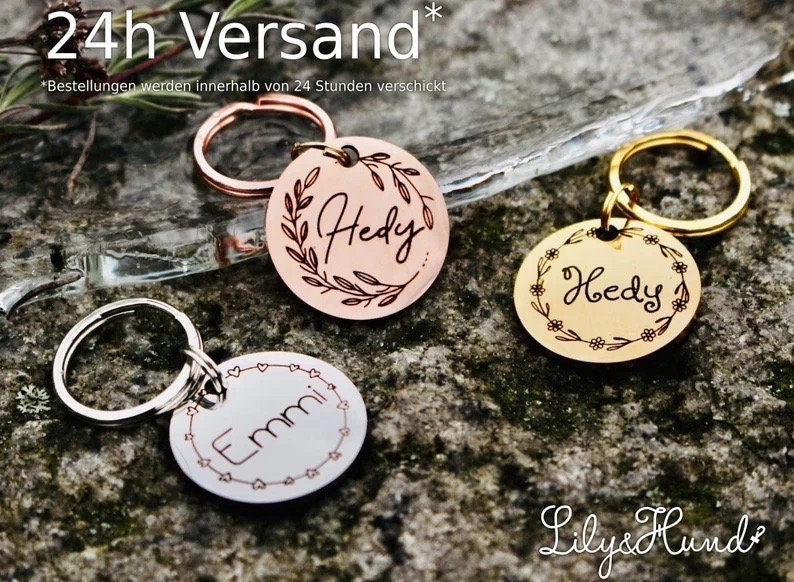 May include: Three personalized dog tag keychains with different designs. The keychains are made of metal and have a round shape. The first keychain has a copper finish with a wreath design and the name "Hedy" engraved on it. The second keychain has a gold finish with a floral design and the name "Hedy" engraved on it. The third keychain has a silver finish with a heart design and the name "Emmi" engraved on it. The keychains are displayed on a textured surface.