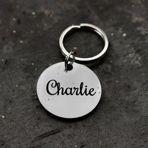 May include: Silver dog tag with a black engraved name "Charlie" attached to a silver key ring.