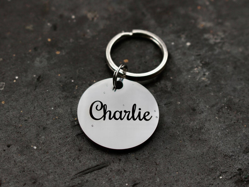 May include: Silver dog tag with a black engraved name "Charlie" attached to a silver key ring.