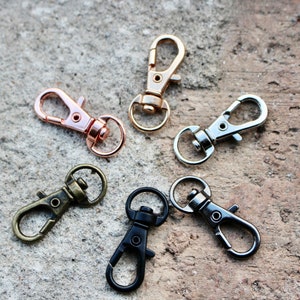 May include: Five metal keychains in different colors. Two are rose gold, one is silver, and two are black.