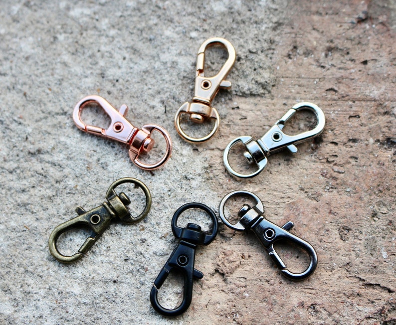 May include: Five metal keychains in different colors. Two are rose gold, one is silver, and two are black.