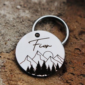 May include: Silver dog tag with a mountain and sun design and the name "Fion" engraved on it.